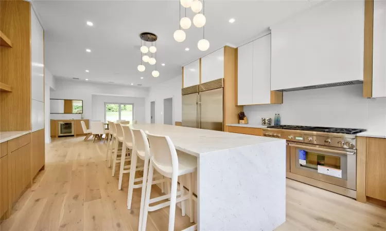 Kitchen with high end appliances, a center island, decorative light fixtures, white cabinets, and light wood-type flooring