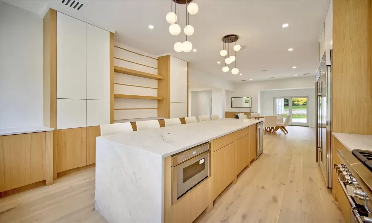 Kitchen featuring white cabinets, light wood-type flooring, decorative light fixtures, a kitchen island, and light stone counters