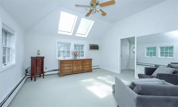 Sitting room with carpet, lofted ceiling with skylight, ceiling fan, baseboard heating, and a wall mounted AC