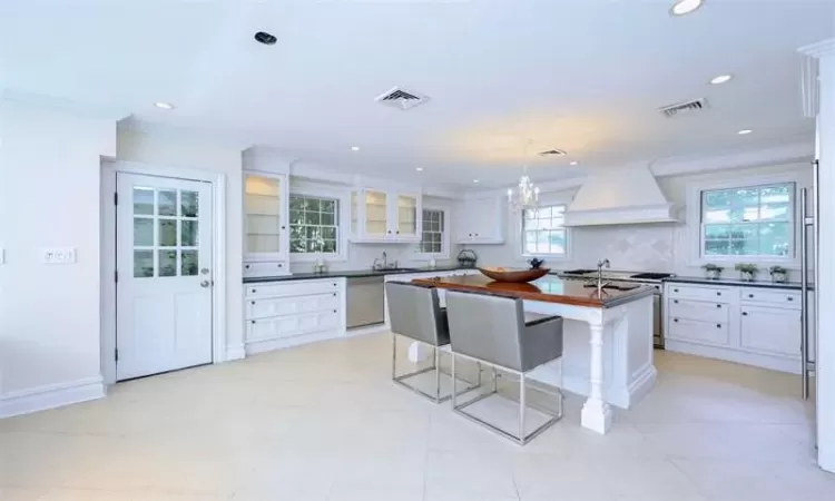 Kitchen with premium range hood, white cabinets, decorative light fixtures, and appliances with stainless steel finishes