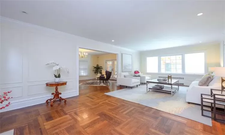 Living room with dark parquet floors, radiator, crown molding, and a notable chandelier