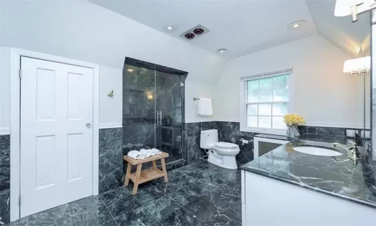 Bathroom with radiator heating unit, vaulted ceiling, tiled shower, toilet, and tile walls