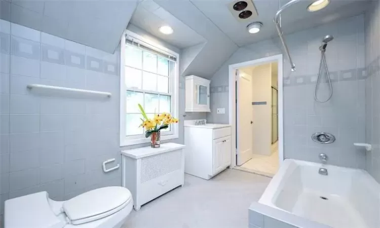 Full bathroom with vanity, toilet, tile walls, and tiled shower / bath