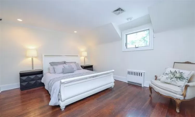 Bedroom featuring vaulted ceiling, radiator heating unit, and dark hardwood / wood-style floors