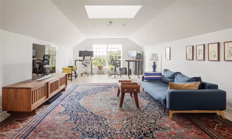 Living room with vaulted ceiling with skylight and light hardwood / wood-style floors