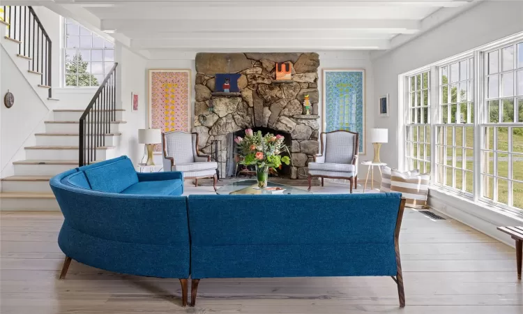 Living room with beam ceiling, light wood-type flooring, a fireplace, and a wealth of natural light