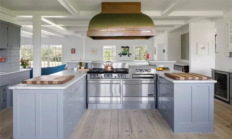 Kitchen with stainless steel range with gas cooktop, a kitchen island, a healthy amount of sunlight, custom range hood, and beverage cooler