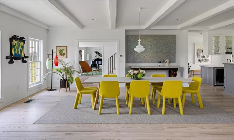 Dining space with beamed ceiling, beverage cooler, and light wood-type flooring