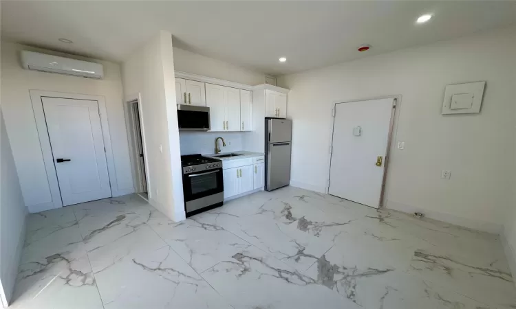 Kitchen featuring an AC wall unit, white cabinetry, sink, and stainless steel appliances