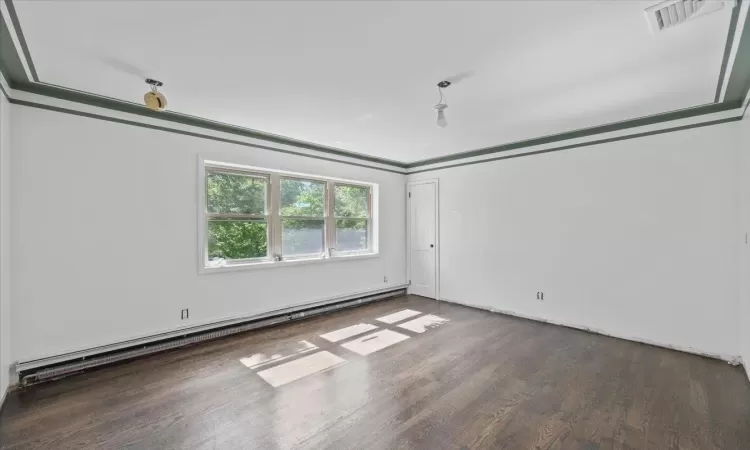 Empty room featuring dark hardwood / wood-style flooring and a baseboard radiator