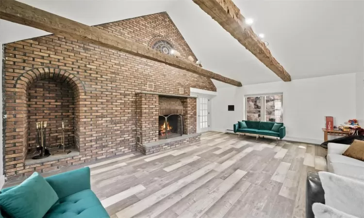 Unfurnished living room featuring hardwood / wood-style flooring, lofted ceiling with beams, a fireplace, and brick wall