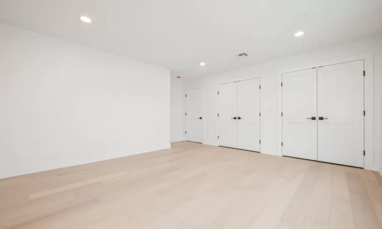 Primary bedroom with light hardwood flooring and multiple closets