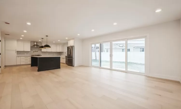 Kitchen with a center island, hanging light fixtures, wall chimney exhaust hood, stainless steel fridge, and white cabinetry