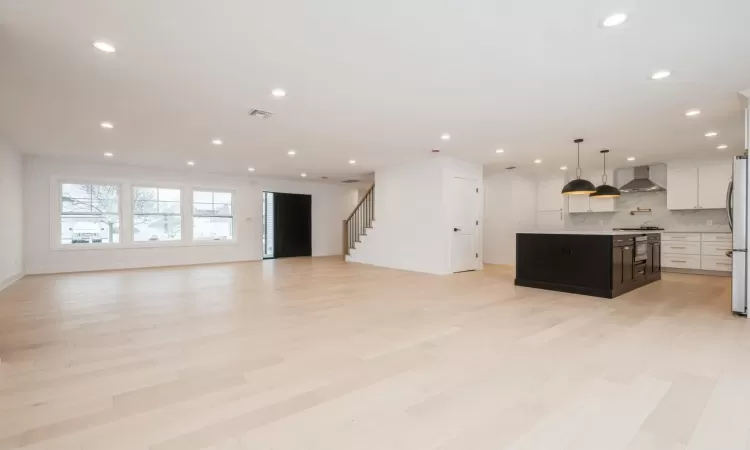 Kitchen featuring a center island, white cabinets, wall chimney range hood, light hardwood flooring, and decorative quartz backsplash