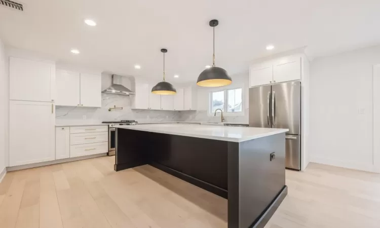 Kitchen with appliances with stainless steel finishes, quartz backsplash, wall chimney exhaust hood, white cabinets, and a center island