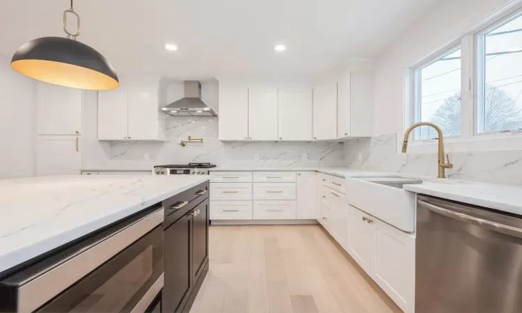 Kitchen featuring light quartz countertops, dishwasher, wall chimney exhaust hood, pendant lighting, and white cabinets