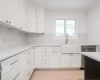 Kitchen with white cabinets, backsplash, light quartz counters, and sink