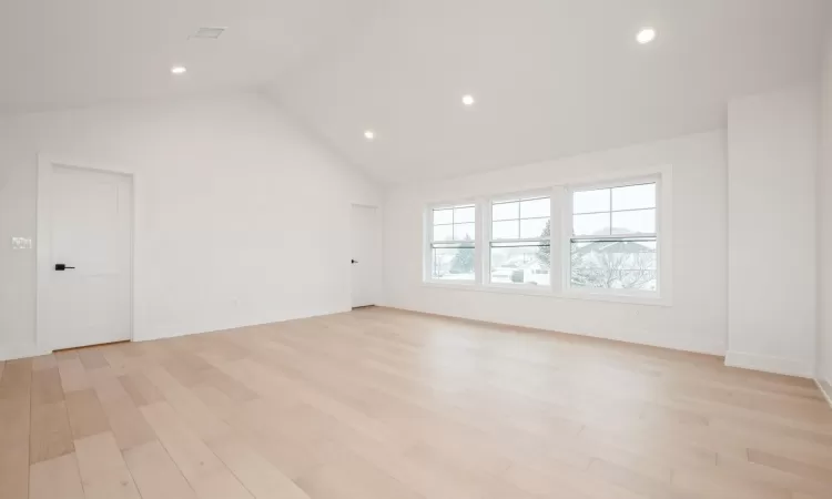 Primary Bedroom w light hardwood floors and vaulted ceiling