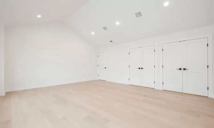 Primary bedroom featuring multiple closets, light hardwood flooring, and lofted ceiling