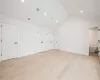 Primary bedroom with vaulted ceiling, ensuite bath, two closets, and light hardwood flooring