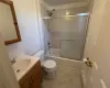 Full bathroom featuring baseboard heating, tile patterned flooring, combined bath / shower with glass door, toilet, and vanity