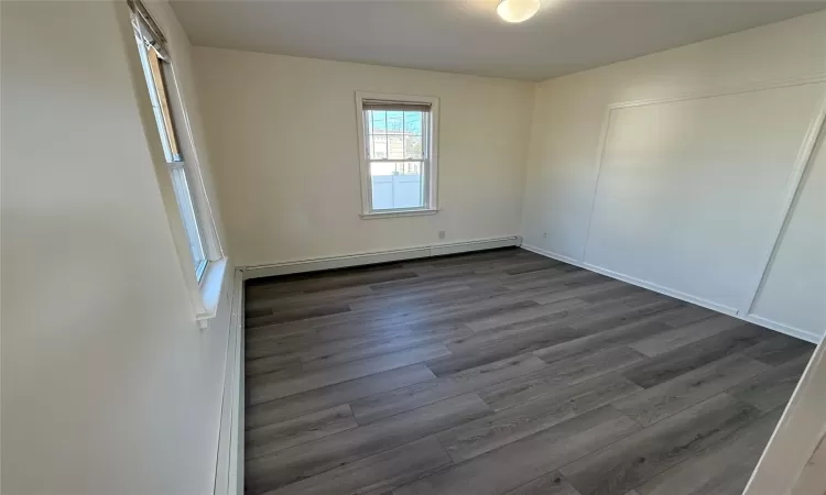 Unfurnished room featuring dark wood-type flooring and a baseboard radiator