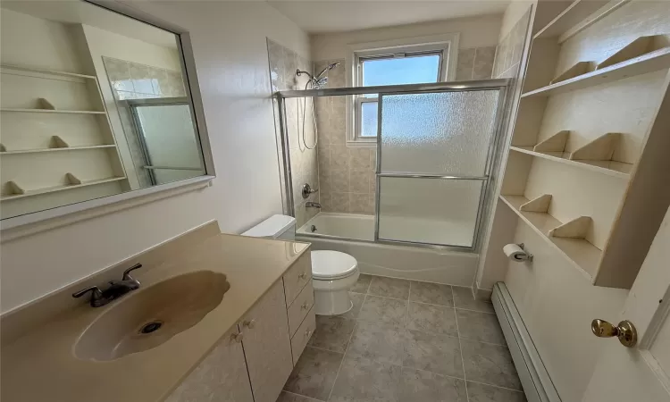 Full bathroom with vanity, a baseboard radiator, toilet, and bath / shower combo with glass door