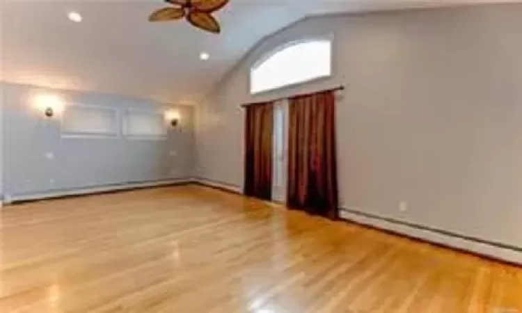 Empty room with ceiling fan, light hardwood / wood-style floors, lofted ceiling, and baseboard heating