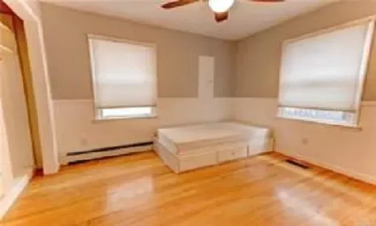 Unfurnished bedroom with ceiling fan, light hardwood / wood-style floors, and a baseboard heating unit