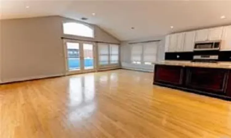 Kitchen with white cabinets, backsplash, light hardwood / wood-style flooring, and lofted ceiling