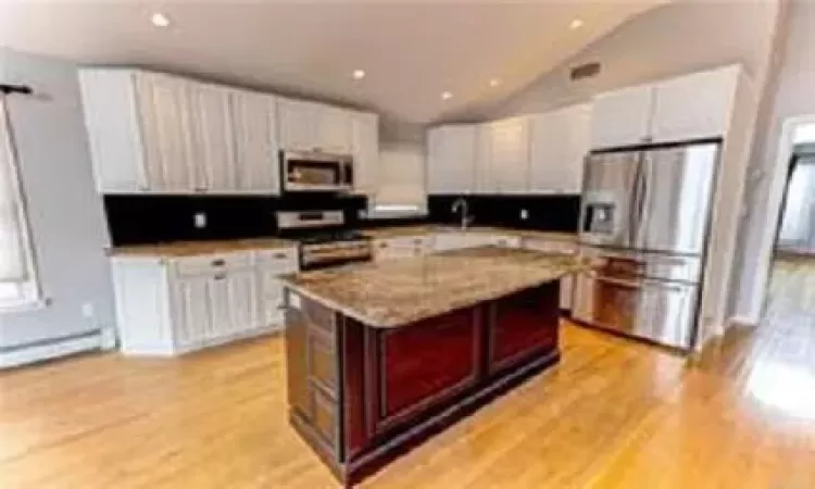 Kitchen featuring a kitchen island, light stone countertops, white cabinetry, and stainless steel appliances