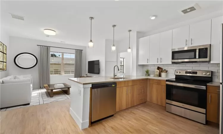 Staged Kitchen featuring stainless steel appliances, sink, decorative light fixtures, light hardwood / wood-style flooring, and white cabinets