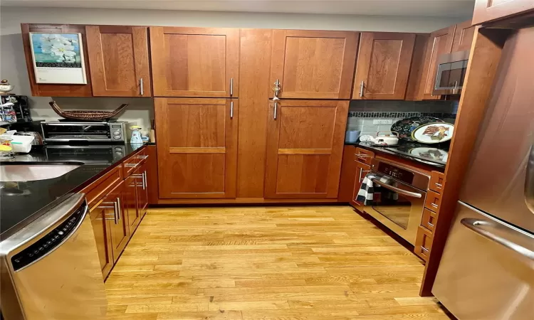 Kitchen with light wood-type flooring Cherry cabinets and granite, sink, appliances with stainless steel finishes, and tasteful backsplash