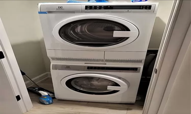 Laundry area with stacked washer / drying machine and light wood-type flooring