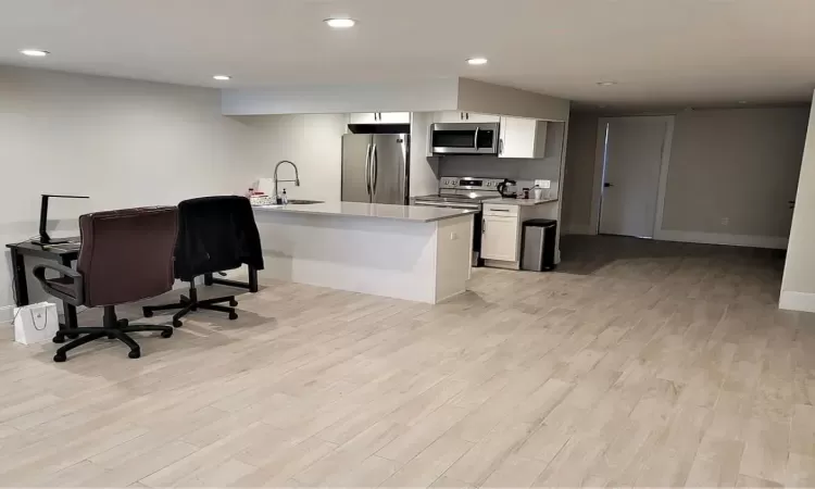 Kitchen featuring a kitchen breakfast bar, sink, light hardwood / wood-style floors, white cabinetry, and stainless steel appliances