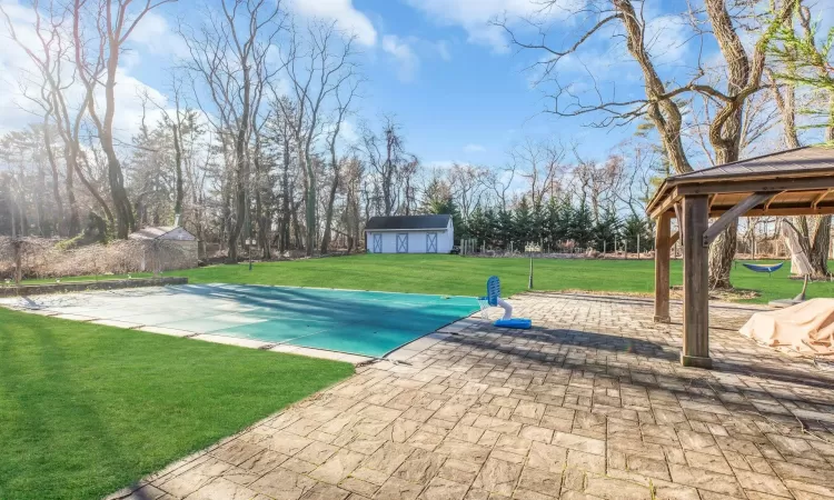 View of pool featuring a lawn, a storage unit, a gazebo, and a patio area