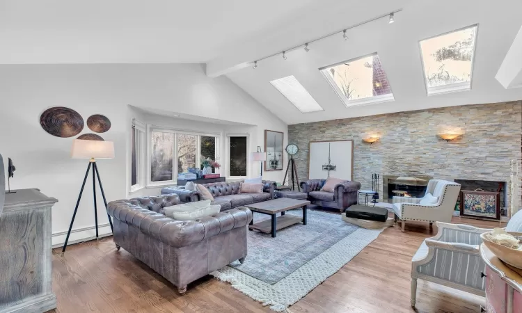 Living room with a skylight, rail lighting, a baseboard radiator, a fireplace, and hardwood / wood-style flooring