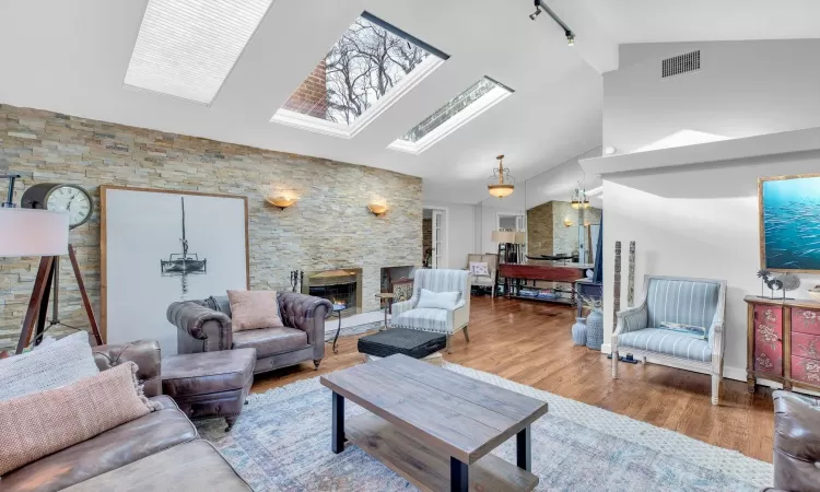 Living room with a skylight, rail lighting, a stone fireplace, high vaulted ceiling, and hardwood / wood-style floors