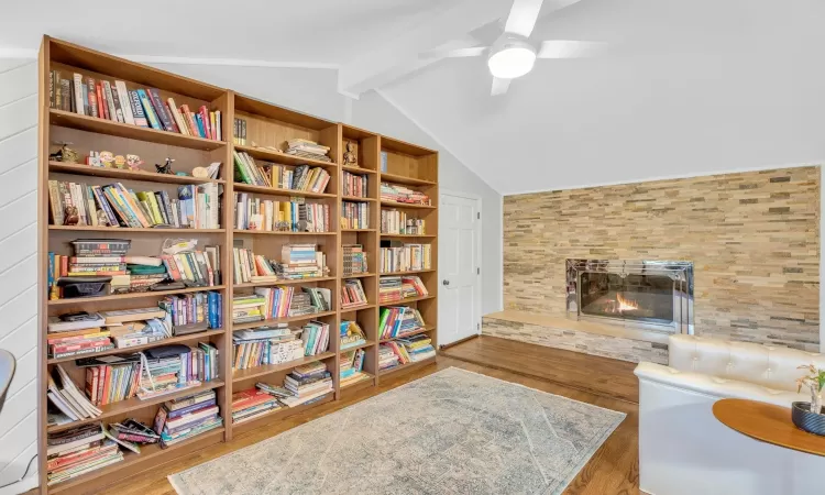 Living area with vaulted ceiling with beams, light hardwood / wood-style floors, a stone fireplace, and ceiling fan