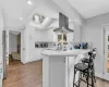 Kitchen with white cabinets, a kitchen breakfast bar, wall chimney exhaust hood, light wood-type flooring, and kitchen peninsula