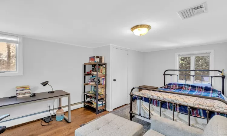 Bedroom featuring hardwood / wood-style floors, crown molding, and a baseboard heating unit