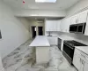 Kitchen featuring appliances with stainless steel finishes, light stone counters, a wall mounted AC, a center island, and white cabinetry