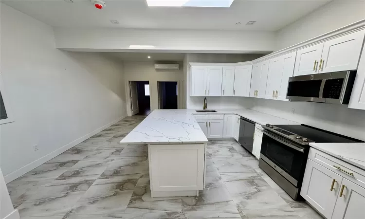 Kitchen featuring appliances with stainless steel finishes, light stone counters, a wall mounted AC, a center island, and white cabinetry