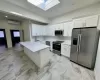 Kitchen featuring a skylight, light stone counters, stainless steel appliances, an AC wall unit, and white cabinetry