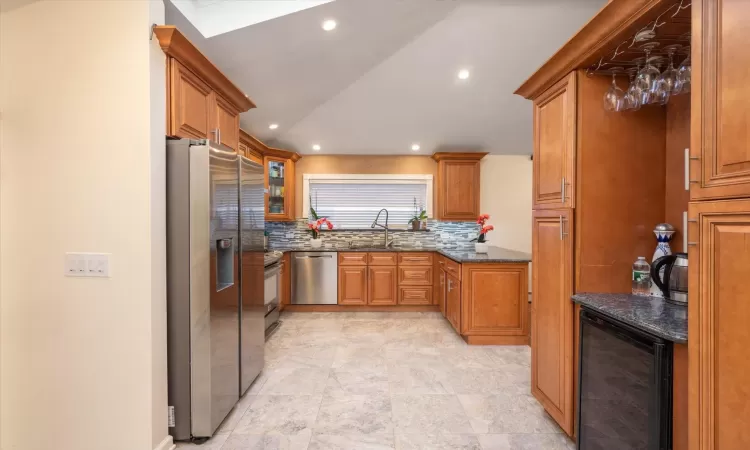 Kitchen featuring sink, stainless steel appliances, wine cooler, backsplash, and dark stone counters