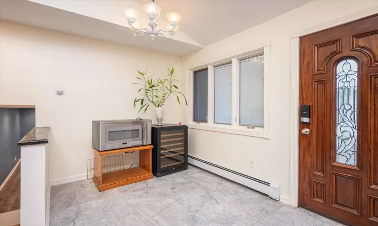 Entrance foyer featuring baseboard heating, a chandelier, and vaulted ceiling