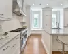 Kitchen featuring wall chimney exhaust hood, white cabinetry, double oven range, and light stone countertops