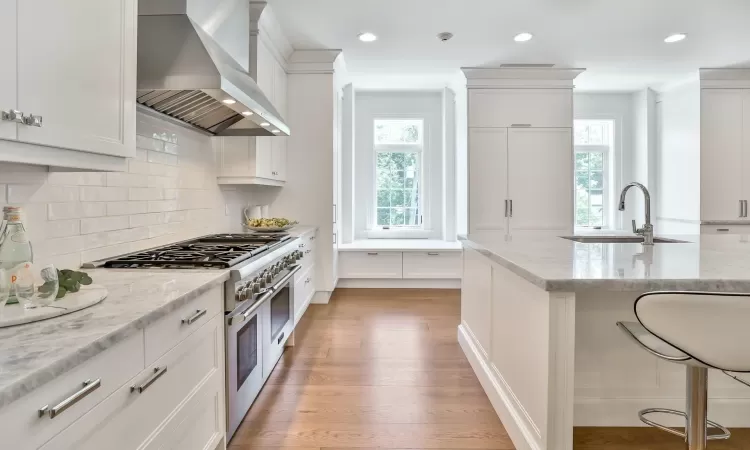 Kitchen featuring wall chimney exhaust hood, white cabinetry, double oven range, and light stone countertops