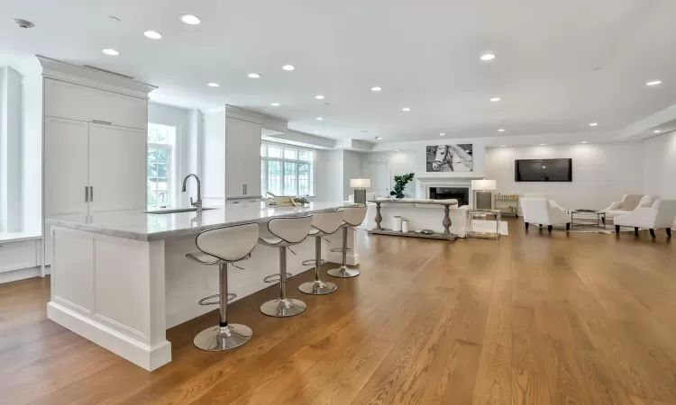 Kitchen with white cabinetry, light stone counters, a large island with sink, a kitchen bar, and light wood-type flooring