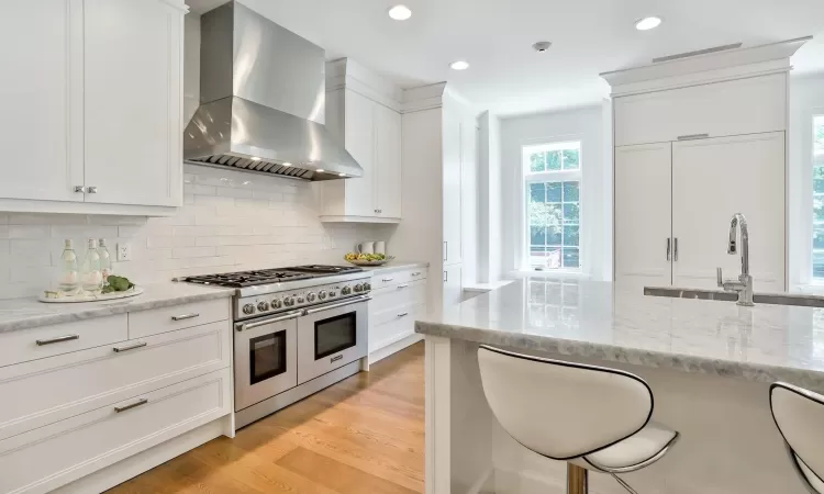 Kitchen with white cabinets, range with two ovens, wall chimney range hood, and light wood-type flooring